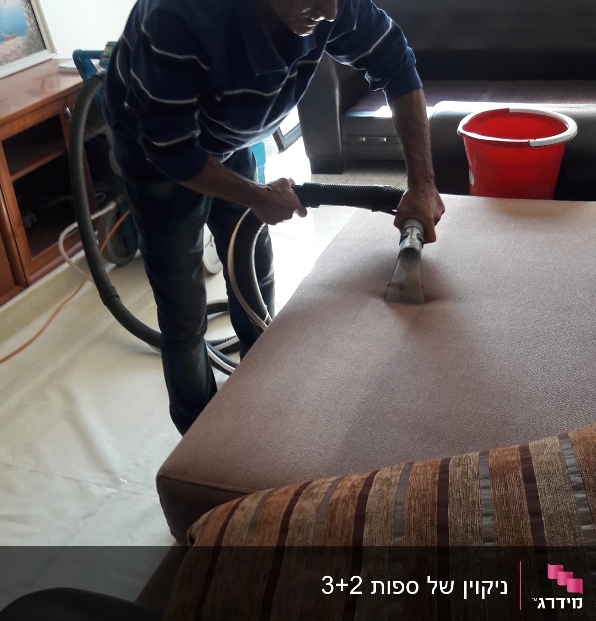 אדם מנקה ספה עם שואב אבק, דלי אדום לידו